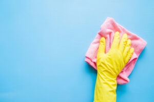 Does an AC Kill Mold? Photo of a hand in a yellow rubber glove wiping a blue wall or table with a pink cloth.