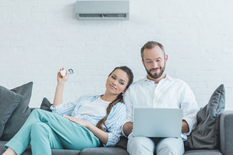 couple sitting on couch turning on ductless AC with remote.