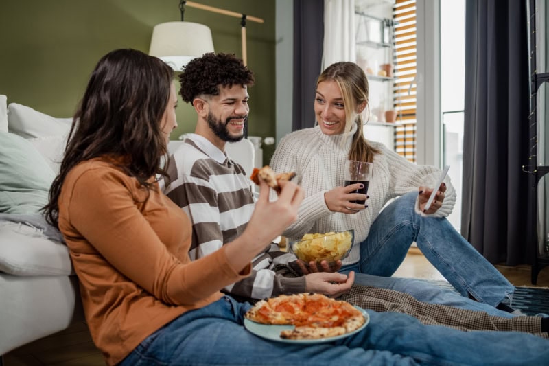 How Do I Know When I Need a New Furnace? Group of friends having a joyful weekend. They are sitting on the floor, eating, drinking and talking.
