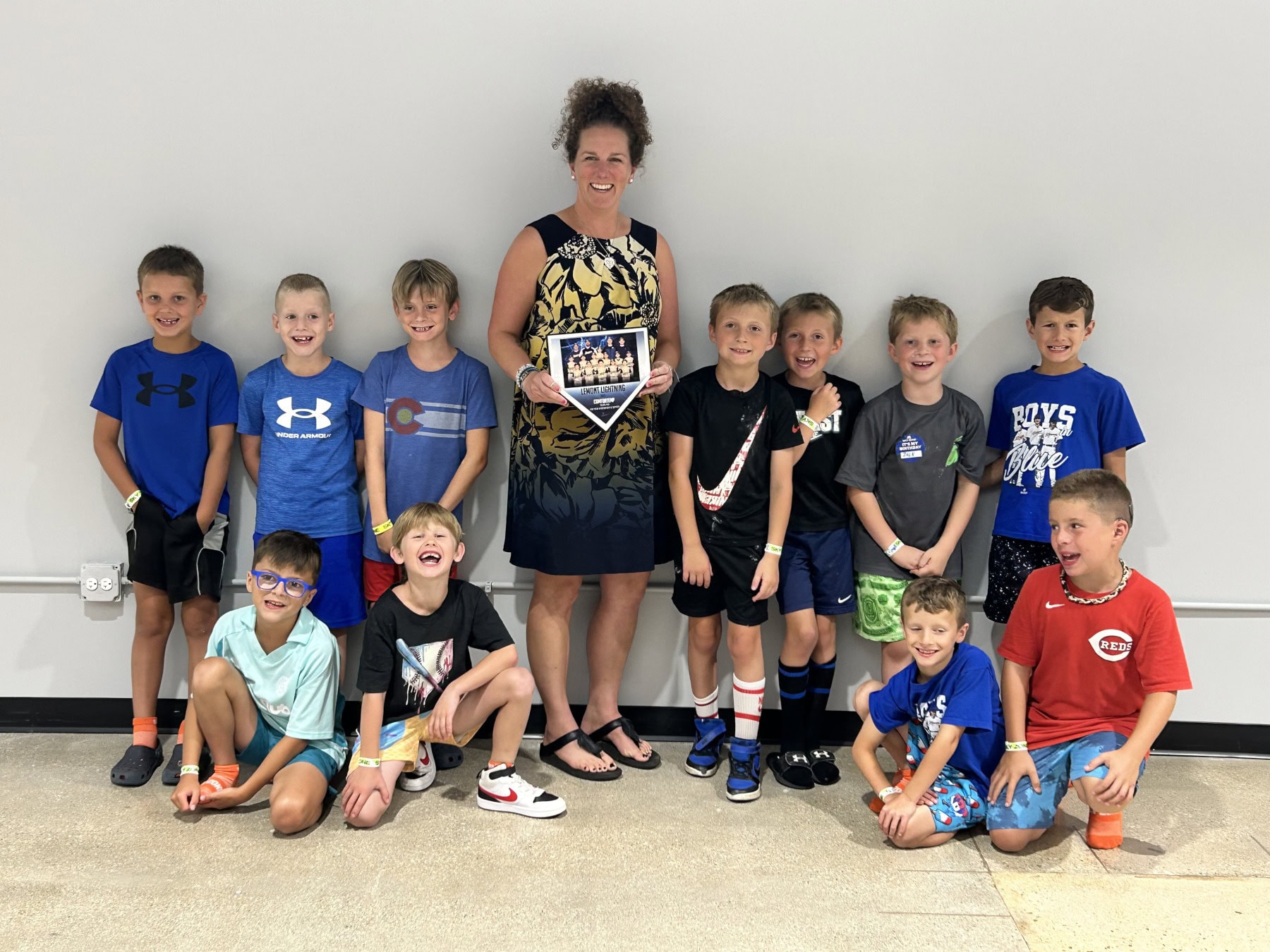 Teacher holding up team picture of the Lemont Lightning Baseball team with players surrounding her in regular clothes.